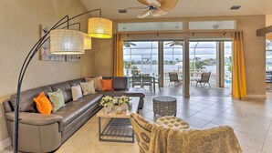 A spacious living area with a sofa, coffee table, and patterned ottoman. A ceiling fan and pendant lights are visible.