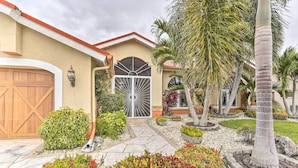 A residential property with a large garage, a gated entrance, and a landscaped garden with palm trees and shrubs.