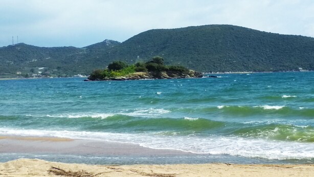A beach with clear water, a sandy shore, and a small island with greenery.
