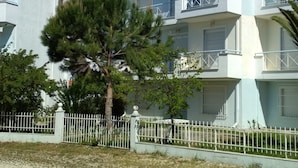 A multi-story building with balconies, a fenced area, and a tree in front.