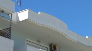 A multi-story building with balconies, air conditioning units, and a clear blue sky.
