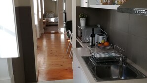 A modern kitchen with a stainless steel sink, a microwave, and a toaster. There is a window providing natural light and a view into the living area. - Ah33 - Superior Family Apartment - University and Historic Center (Coimbra)