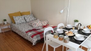 A cozy bedroom with a bed, bedside table, and a dining area with chairs, a table, and breakfast items. - Ah33 - Superior Family Apartment - University and Historic Center (Coimbra)