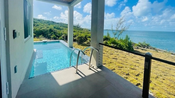 A pool area with a view of the ocean and hills. - High-end New Home - Large PRIVATE Pool, Snorkeling, Cliff Jumping, Kayaks & SUP (Eleuthera)