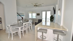 A modern kitchen with a central island, white chairs, and a dining table. - High-end New Home - Large PRIVATE Pool, Snorkeling, Cliff Jumping, Kayaks & SUP (Eleuthera)