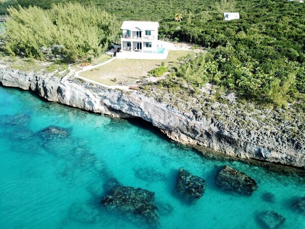 A coastal property with a white building, clear turquoise waters, and rocky cliffs. - High-end New Home - Large PRIVATE Pool, Snorkeling, Cliff Jumping, Kayaks & SUP (Eleuthera)