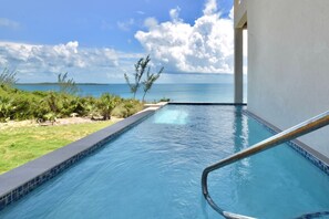 A swimming pool with a view of the ocean, surrounded by greenery and a clear sky. - High-end New Home - Large PRIVATE Pool, Snorkeling, Cliff Jumping, Kayaks & SUP (Eleuthera)