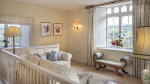 A room with a white sofa, a bench, and a window with curtains. There are two wall-mounted lamps and framed pictures. - Spacious, self contained flat within this Historic Castle of Caerhays, within walking distance of th (Saint Austell)