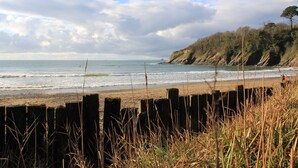 A beach with wooden barriers and grass in the foreground, a sandy shore, and a forested cliff in the background. - Spacious, self contained flat within this Historic Castle of Caerhays, within walking distance of th (Saint Austell)