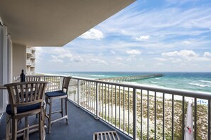 A balcony with two wooden chairs and a table, overlooking a beach with a pier. - Summerwind Resort 602 Center * Beach Chair Set Included * Salt Water Vacations (Navarre)