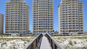 A beachfront hotel with multiple balconies, a boardwalk leading to the beach, and a clear sky. - Summerwind Resort 602 Center * Beach Chair Set Included * Salt Water Vacations (Navarre)