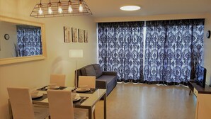 Ein Essbereich mit Tisch für zwei Personen, einer Couch und einem großen Fenster mit gemusterten Vorhängen.