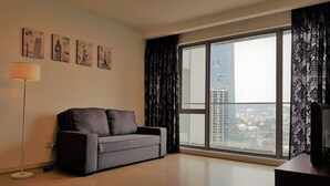 Ein modernes Wohnzimmer mit einem grauen Sofa, einem Flachbildfernseher und einem großen Fenster mit Blick auf die Stadt.