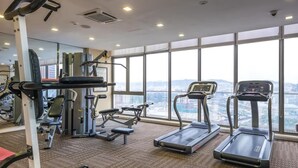 Ein Fitnessstudio mit Laufbändern, Krafttrainingsgeräten und einem großen Fenster mit Blick auf die Stadt.