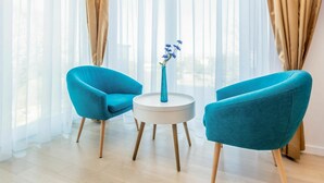 Ein modernes Zimmer mit zwei sesseln in Türkis, einem weißen runden Tisch und einer Vase mit blauen Blumen.