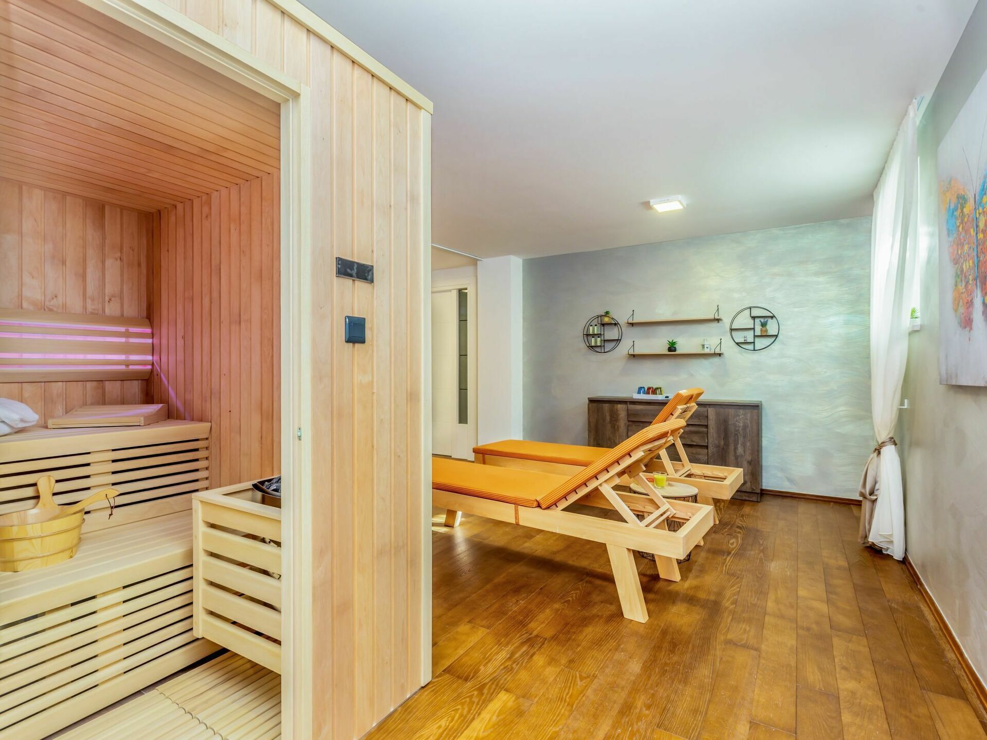 A sauna room with wooden benches and a bench with a towel. There is a wooden cabinet and a shelf with decorative items.