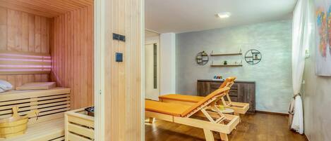 A sauna room with wooden benches and a bench with a towel. There is a wooden cabinet and a shelf with decorative items.