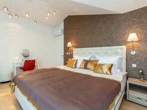 A modern hotel room with a large bed, a red chair, a white desk, and a wall-mounted air conditioner.
