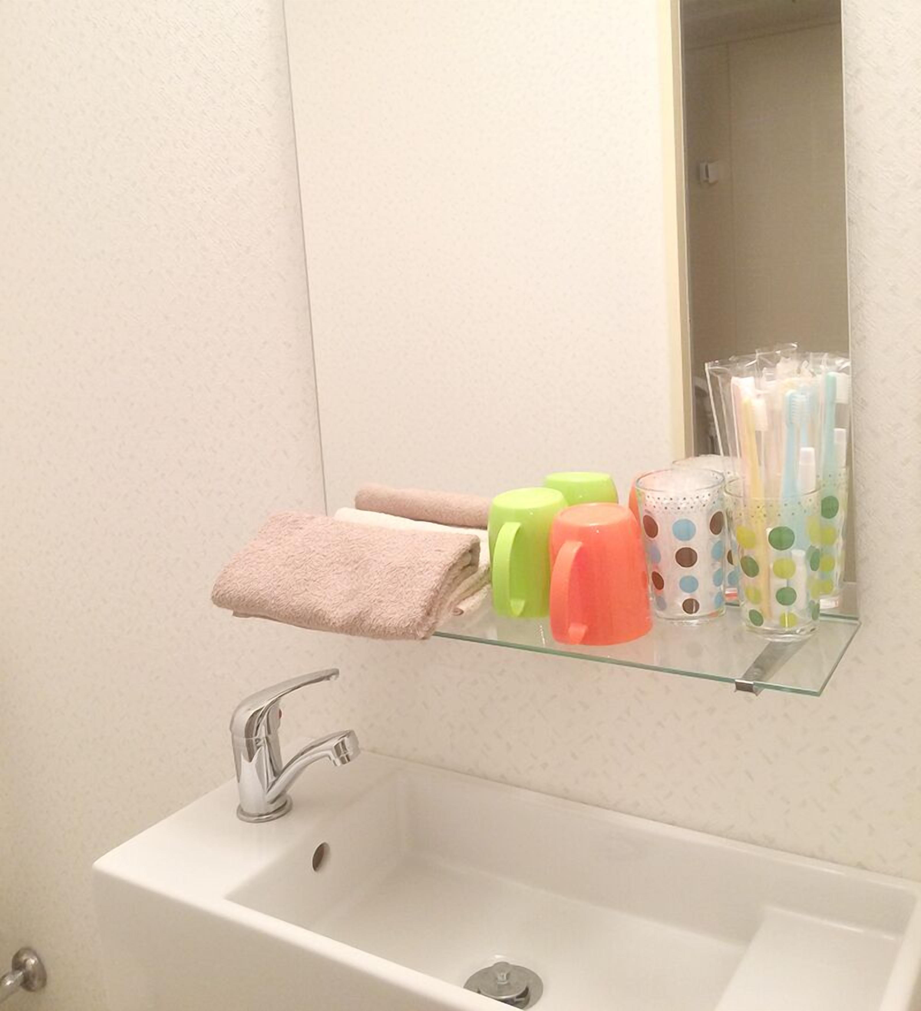 A bathroom with a white sink, a mirror, and a shelf with toiletries.