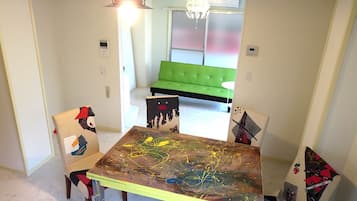 A dining area with a table covered in abstract art, two chairs with colorful patterns, a green sofa in the background, and a chandelier.