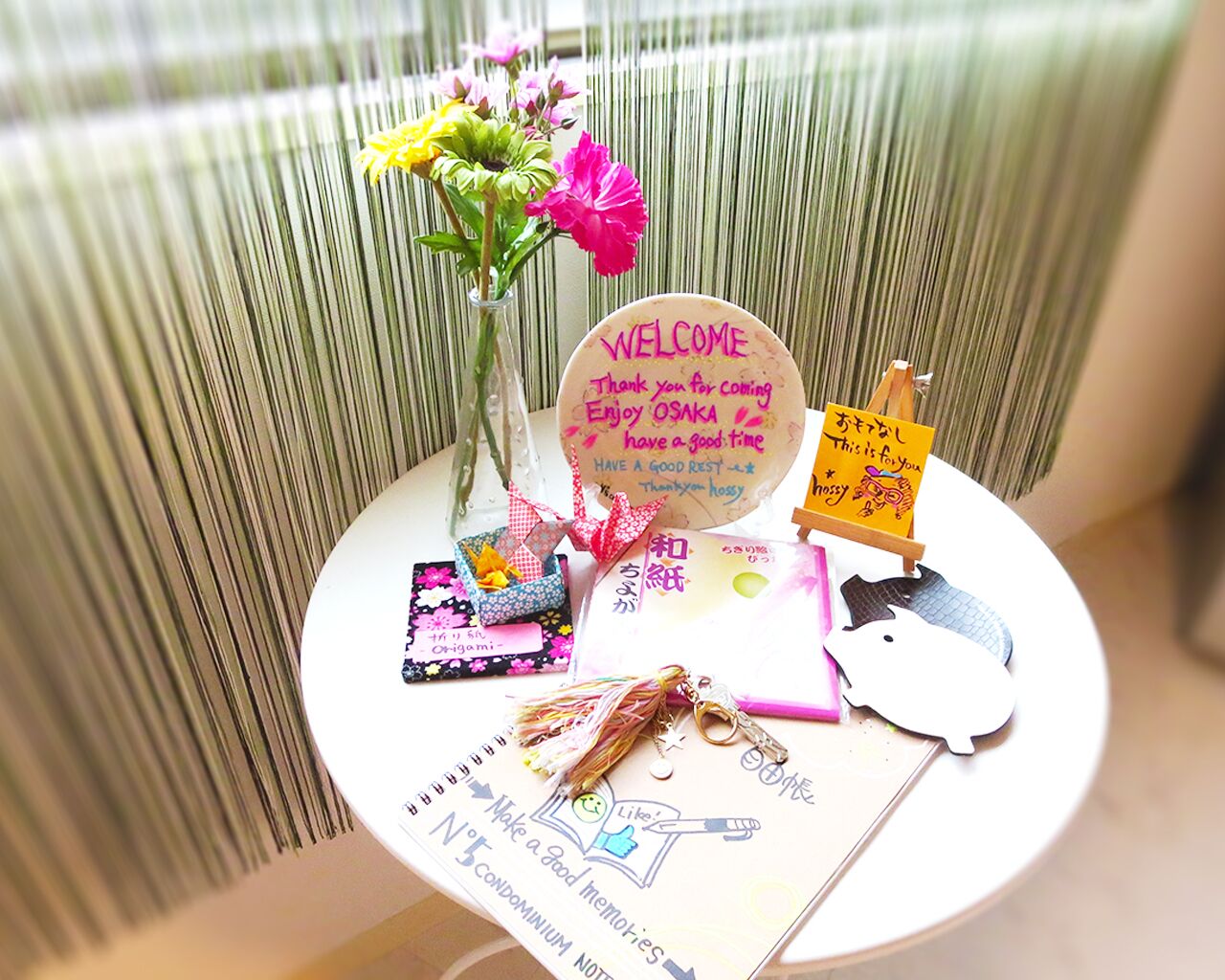 A small table with a welcome sign, origami, a keychain, and a decorative item.