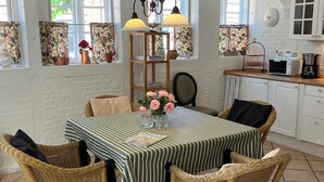 A dining area with a table set for four, surrounded by wicker chairs, a bookshelf, and a window with floral curtains. - Cozy town house in the center of Assens, close to the harbor. (Assens)