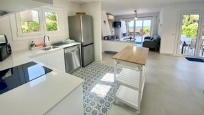 A modern kitchen with a dishwasher, a refrigerator, and a dining area with a table and chairs. - Villenpark Playa Arena House Ocean (Lloret de Mar)