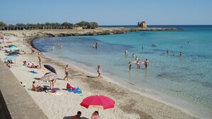 A beach with clear turquoise water, people swimming and sunbathing, and a castle-like structure in the distance. - Villa with large private pool, stunning views, fantastic for cycling/ walking (Martina Franca)