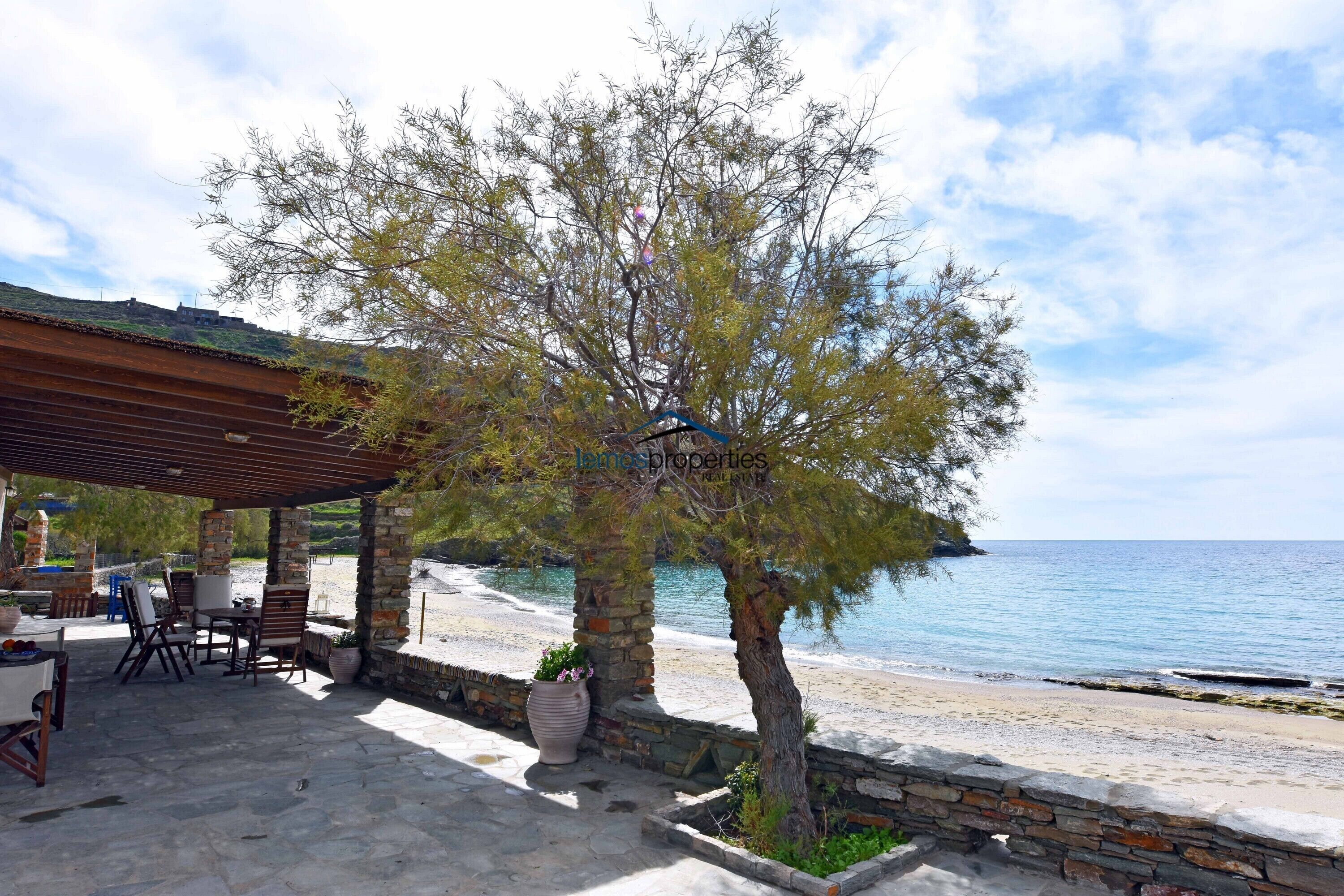 A covered outdoor seating area with stone pillars and a pergola, overlooking a beach.