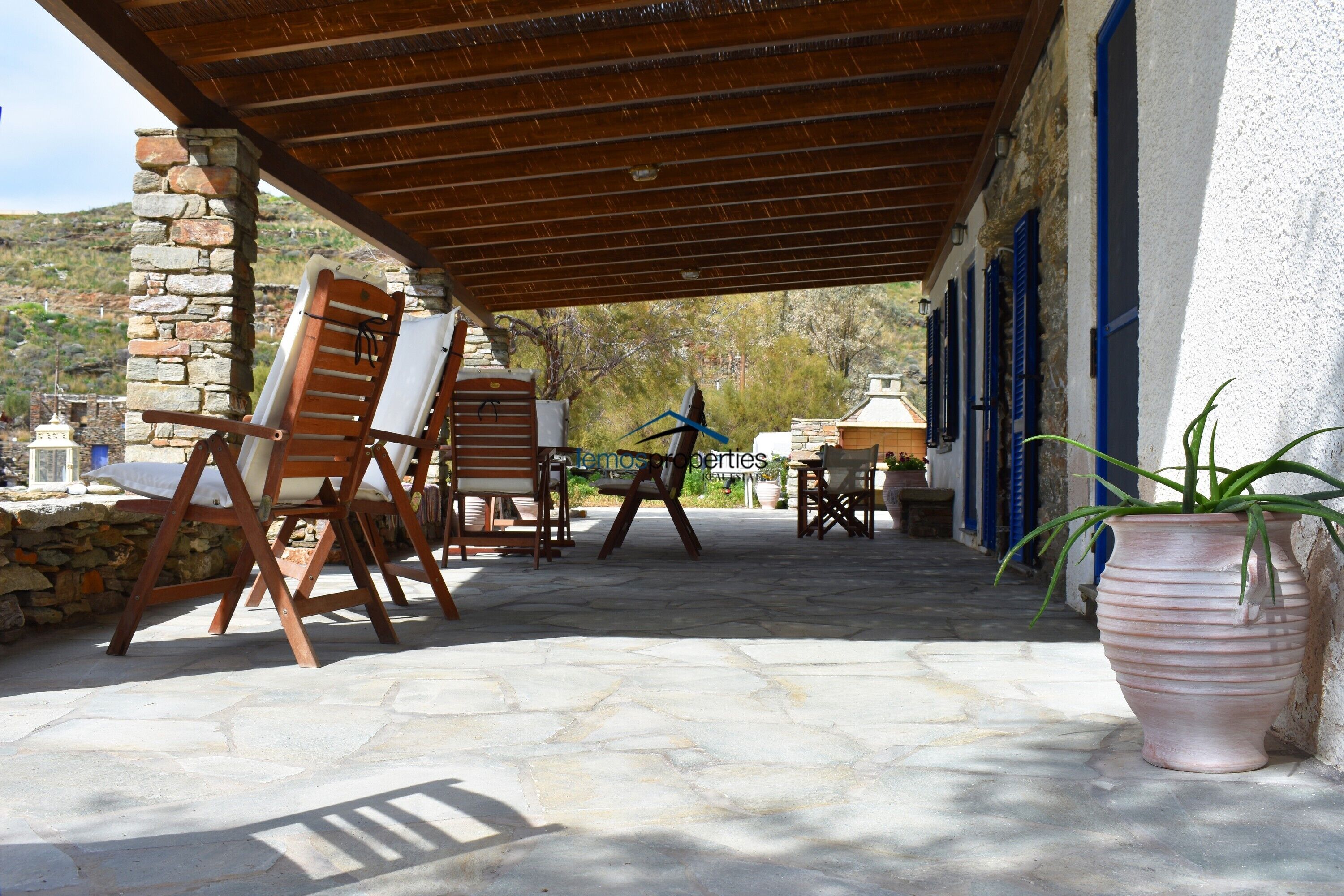 A covered outdoor seating area with stone walls and wooden furniture.