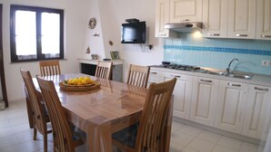 Un coin repas avec une table et des chaises en bois, une cuisine avec des meubles blancs et une cuisinière, et une fenêtre avec des rideaux.