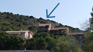 Une colline parsemée de bâtiments, dont une construction à deux étages surmontée d’un toit recouvert de tuiles rouges.