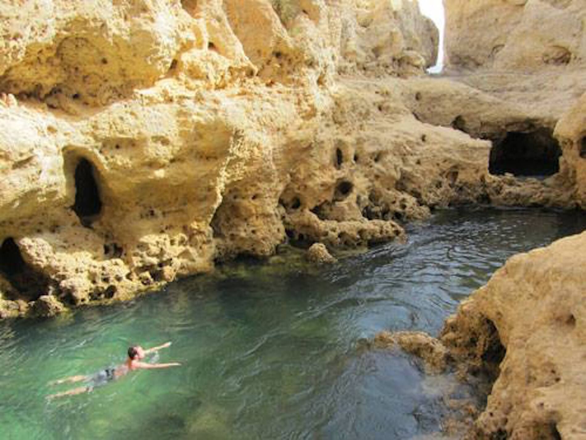 A natural cave with clear water and a person swimming.