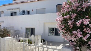 A white building with balconies, a gated entrance, and pink flowering plants.