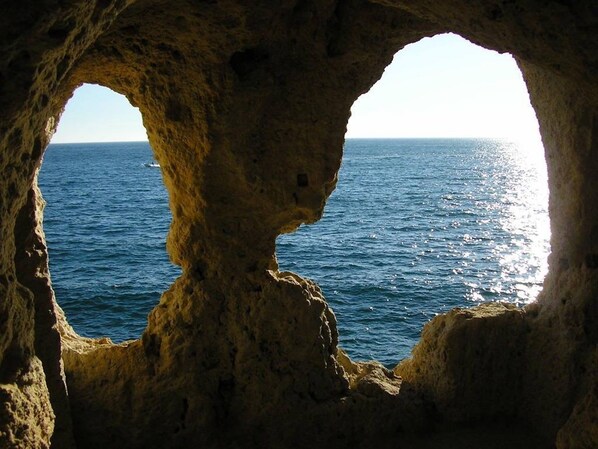 Une vue à travers une arche naturelle formée par la roche, qui surplombe la mer.