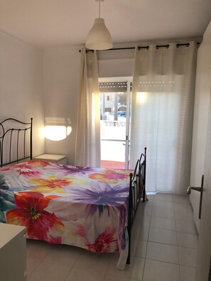 Une chambre à coucher avec un lit, une table de chevet, une lampe suspendue, une fenêtre avec des rideaux et une vue sur la rue.