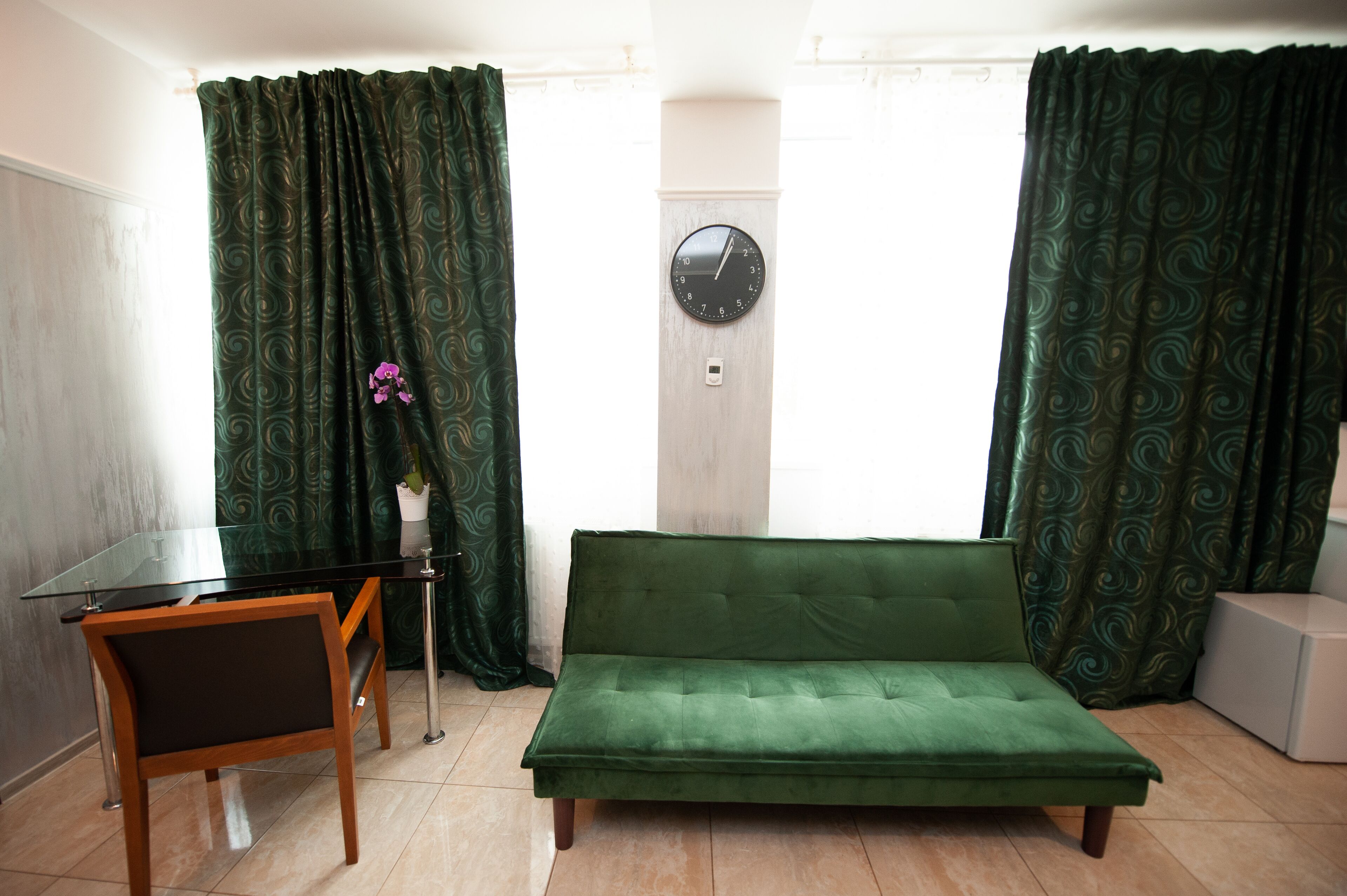 A room with a green sofa, a small table, a chair, and a clock on the wall.