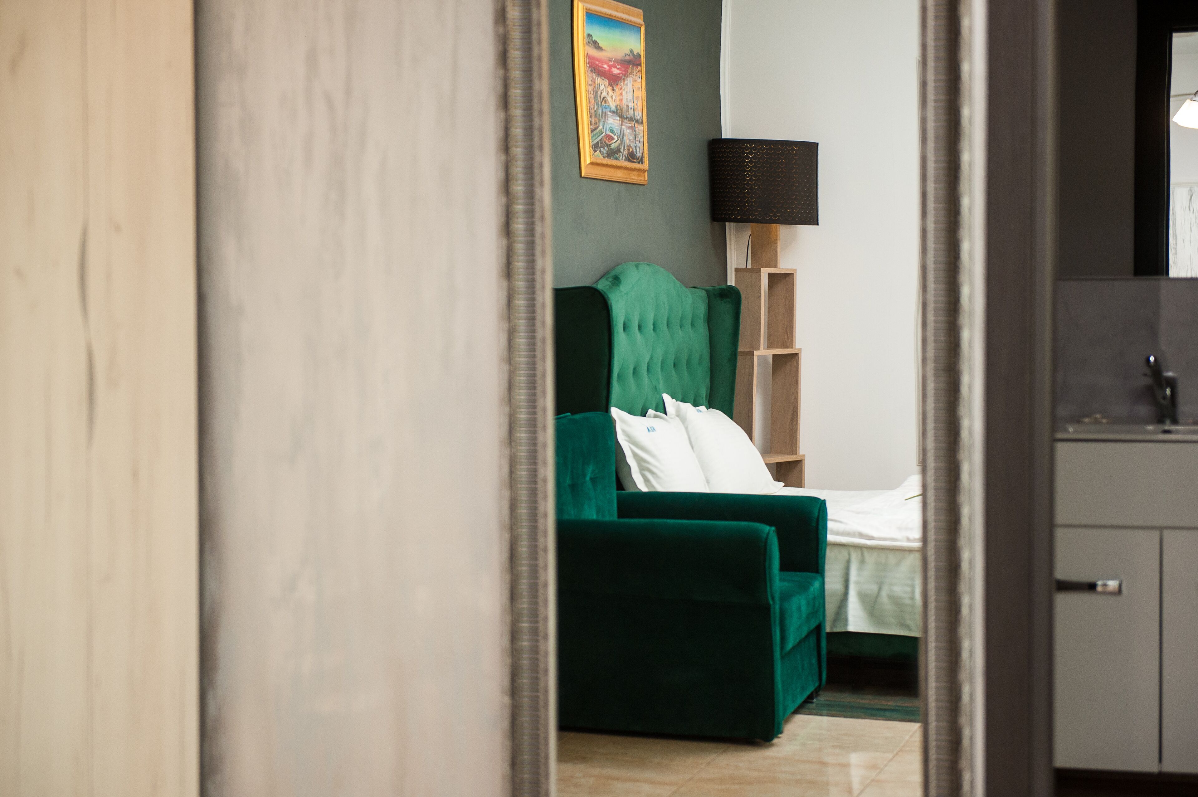 Een kamer met een groene bank, een bed, een houten plankunit en een schilderij aan de muur.