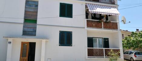 A multi-story building with balconies, a satellite dish, and a car parked nearby.
