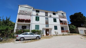 Un immeuble de deux étages doté de balcons, une voiture garée devant, et un ciel bleu dégagé.