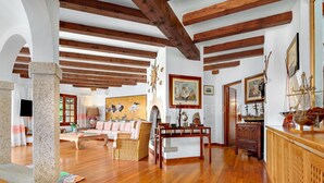 Amplia sala de estar con vigas de madera, un pilar de piedra, un sofá, una mesa de centro y varios objetos decorativos, como pinturas y maquetas de barcos.