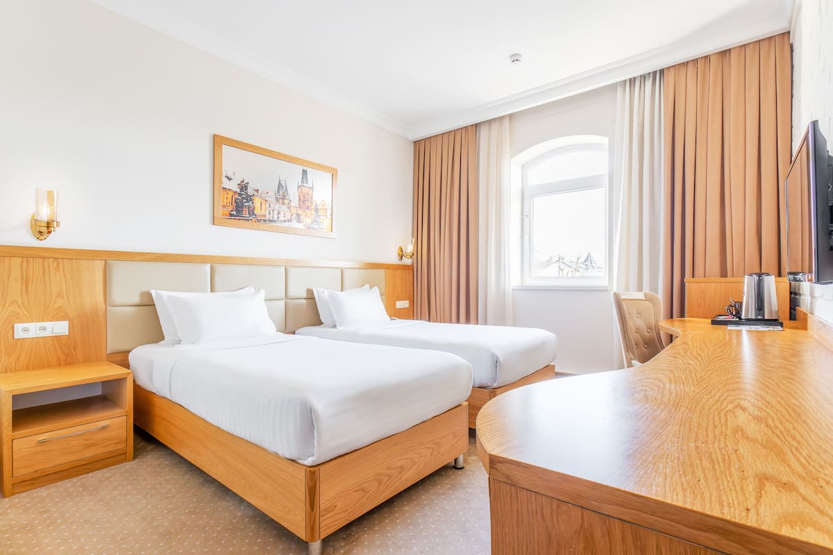 A hotel room with two beds, a wooden desk, a television, and a painting on the wall.