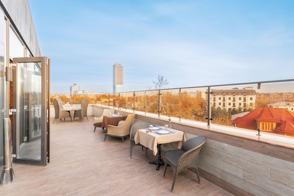 A rooftop terrace with outdoor seating, a glass door entrance, and a view of city buildings.