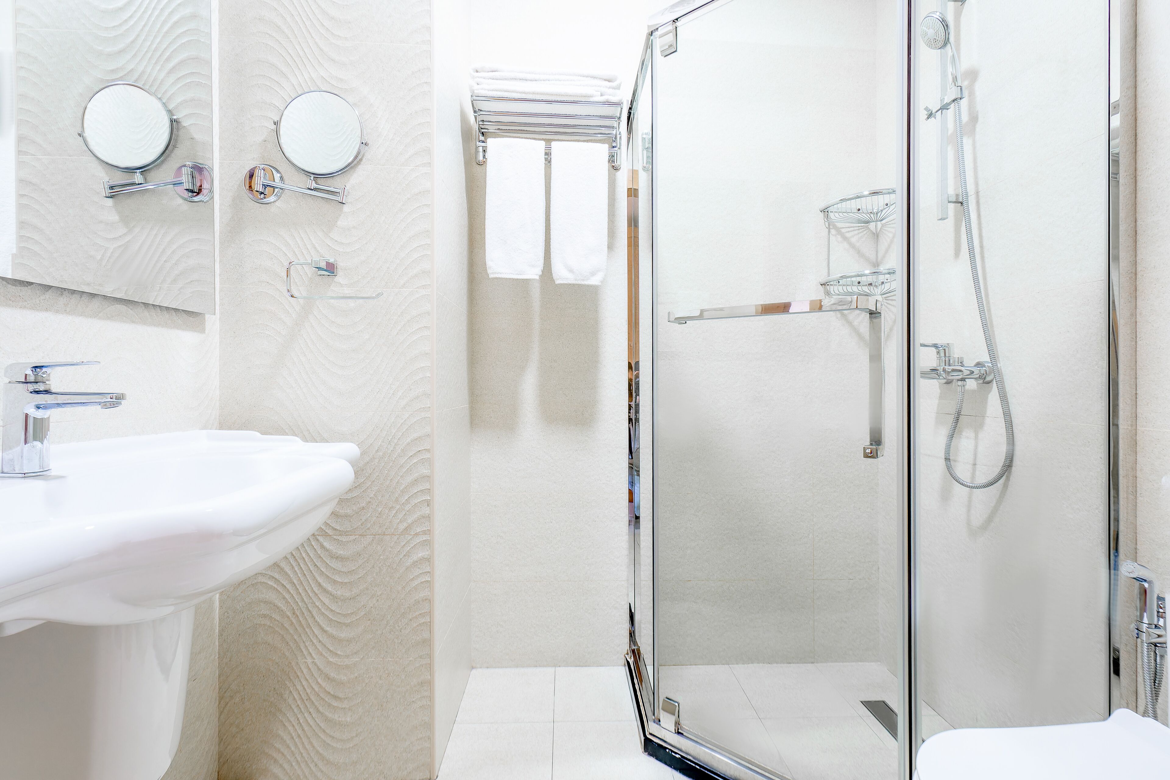 A modern bathroom with a glass-enclosed shower, a white sink, and two mirrors.