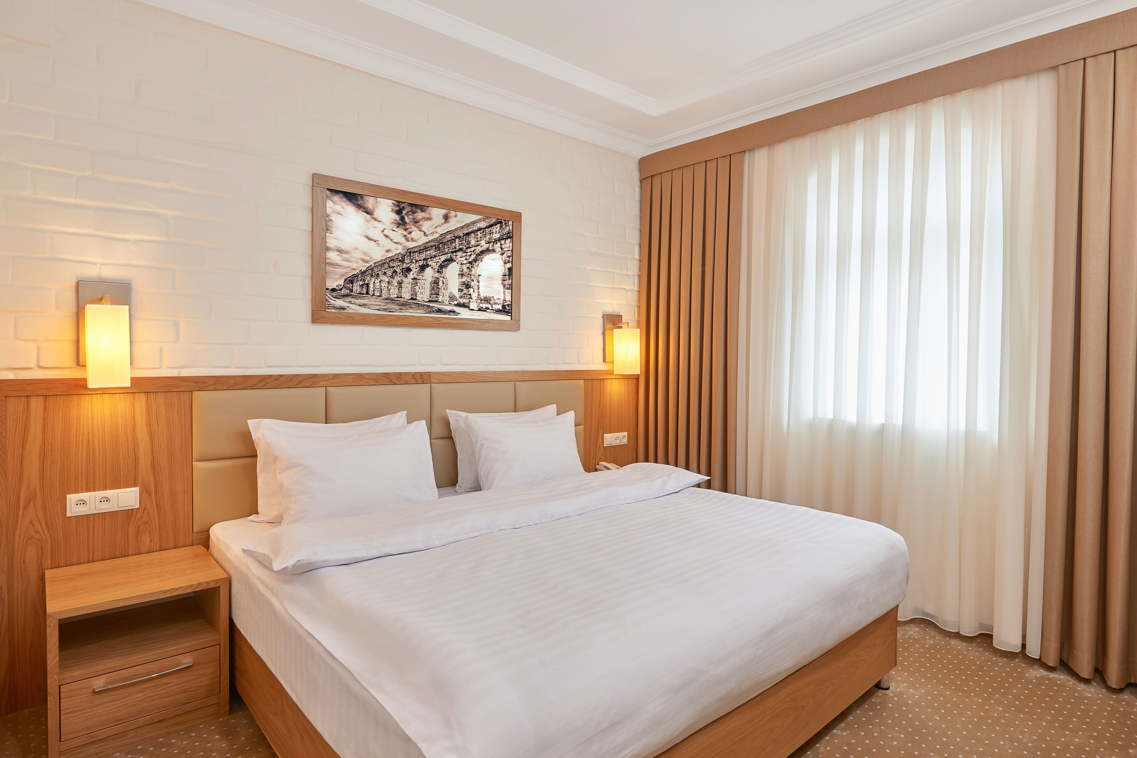 A neatly made bed with a headboard, a bedside table with a lamp, and a framed picture on the wall.