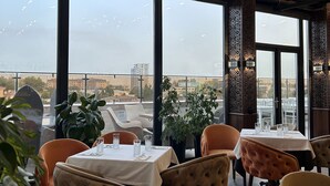 A restaurant with large windows, tables with white tablecloths, and orange chairs. - Praga Hotel (Tashkent)