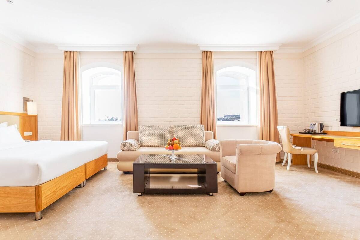 A hotel room with a bed, sofa, armchair, coffee table, and a desk with a TV.