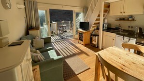 En hyggelig opholdsstue med sofa, et lille bord, et fjernsyn på et træstel og et køkken med vask og komfur.