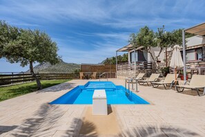 A pool area with a clear blue pool, lounge chairs, and a stone building with a balcony.
