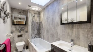 A modern bathroom with a skylight, a bathtub, a toilet, and a large mirror.
